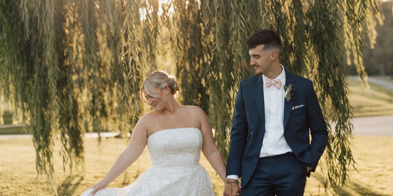 Bride and groom holding hands under a tree's weeping branches