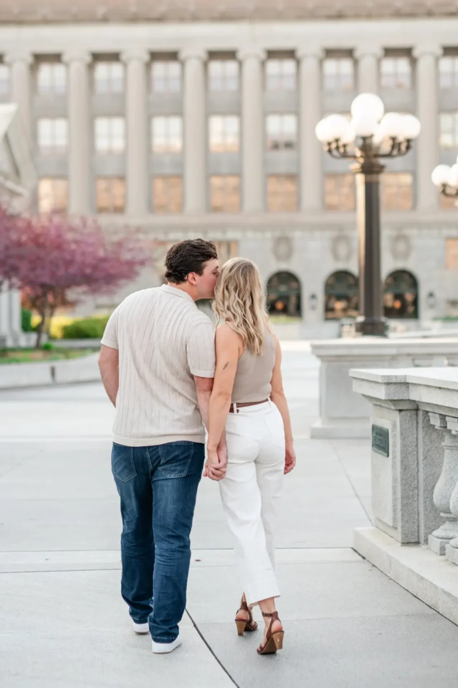 Couple walking hand-in-hand near the Pennsylvania State Capitol, sharing a kiss during their urban engagement session in Harrisburg, PA.