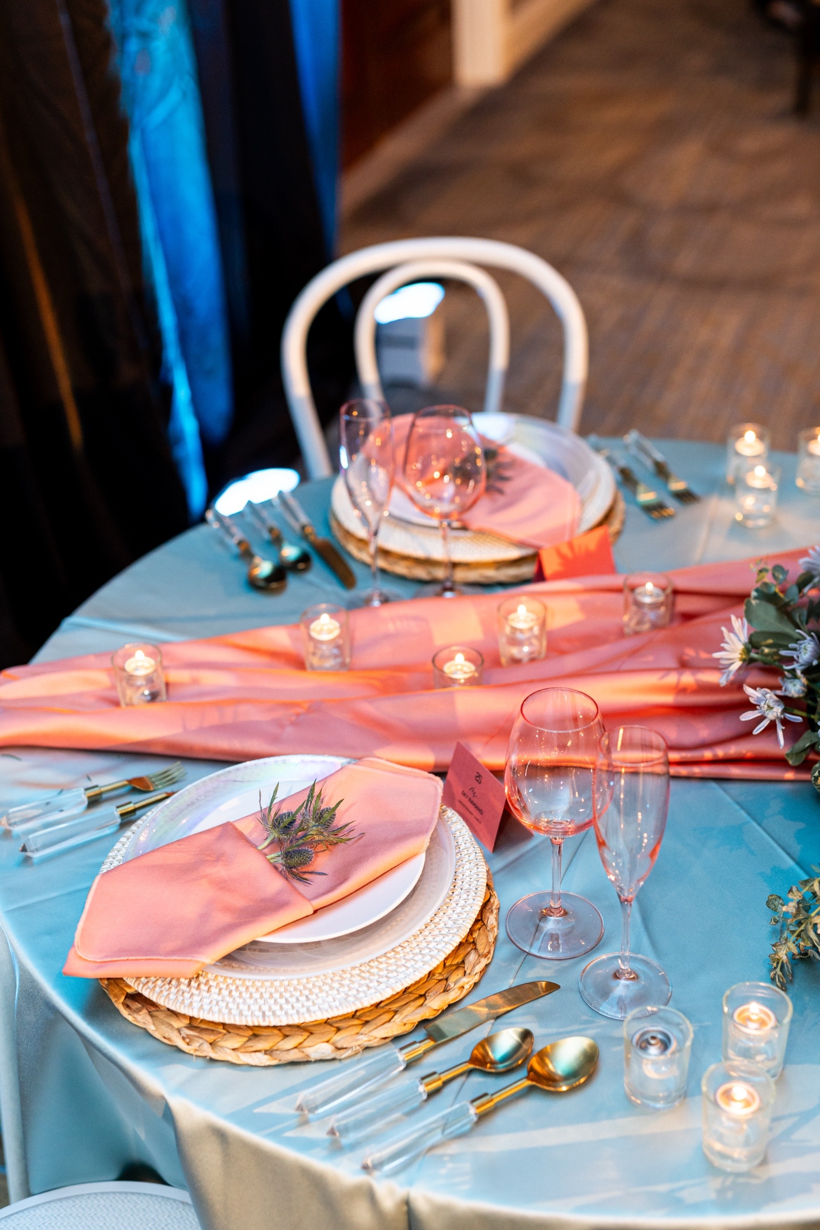 Elegant Mediterranean-inspired wedding tablescape with coral napkins, gold flatware, and blue linens surrounded by candlelight.