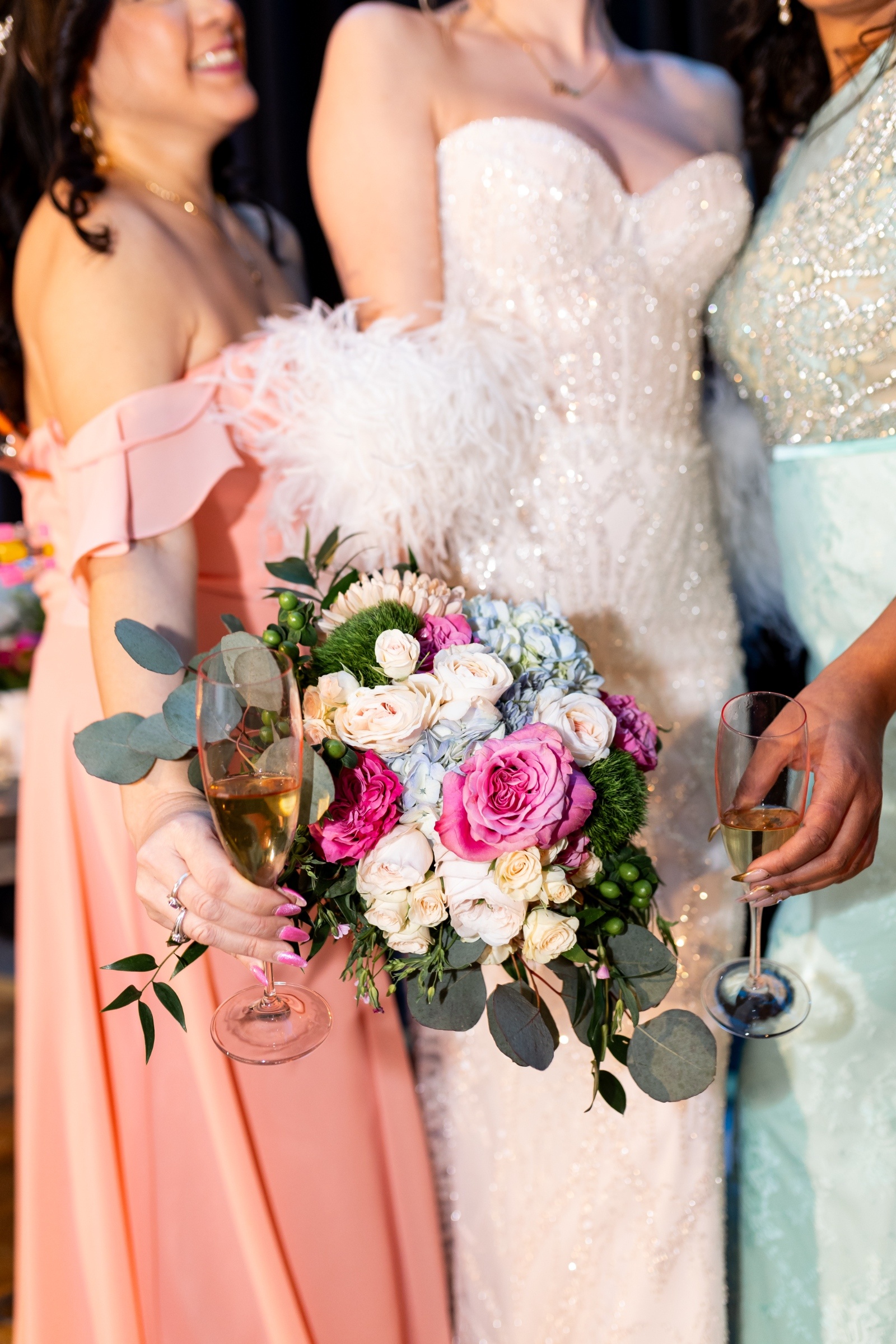 Close-up of bride holding a romantic pink and white bouquet with champagne glasses during wedding celebration.