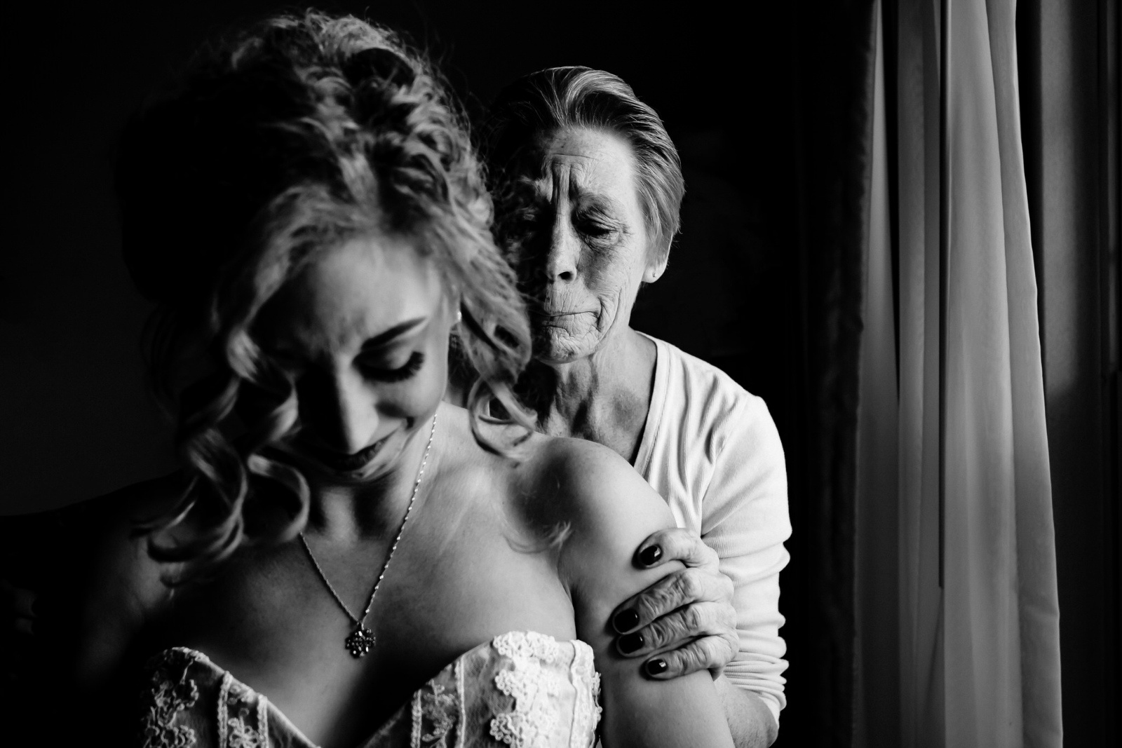 Bride crying with her grandmother crying behind her in black and white