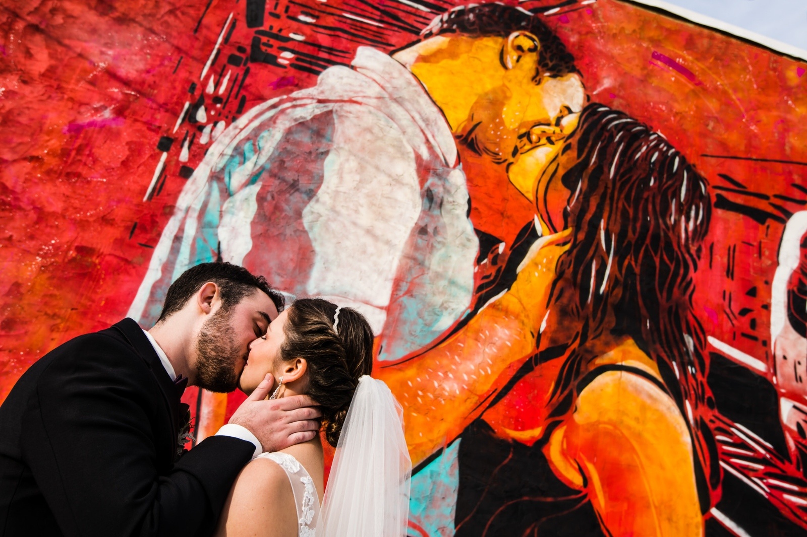 Bride and Groom kissing in front of a colorful mural of a couple kissing