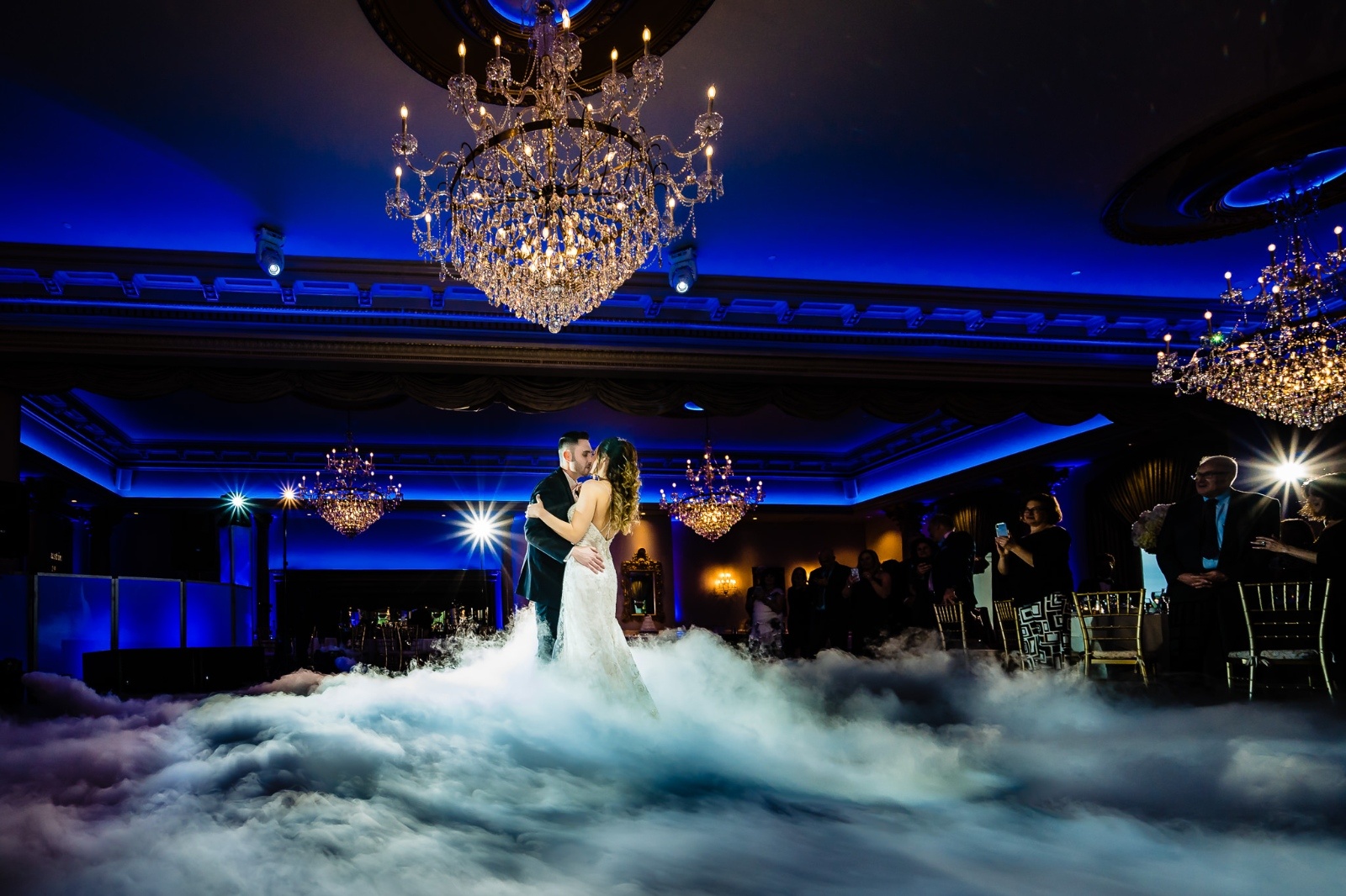 Bride and groom on a dance floor under giant chandelier standing in smoke-filled floor
