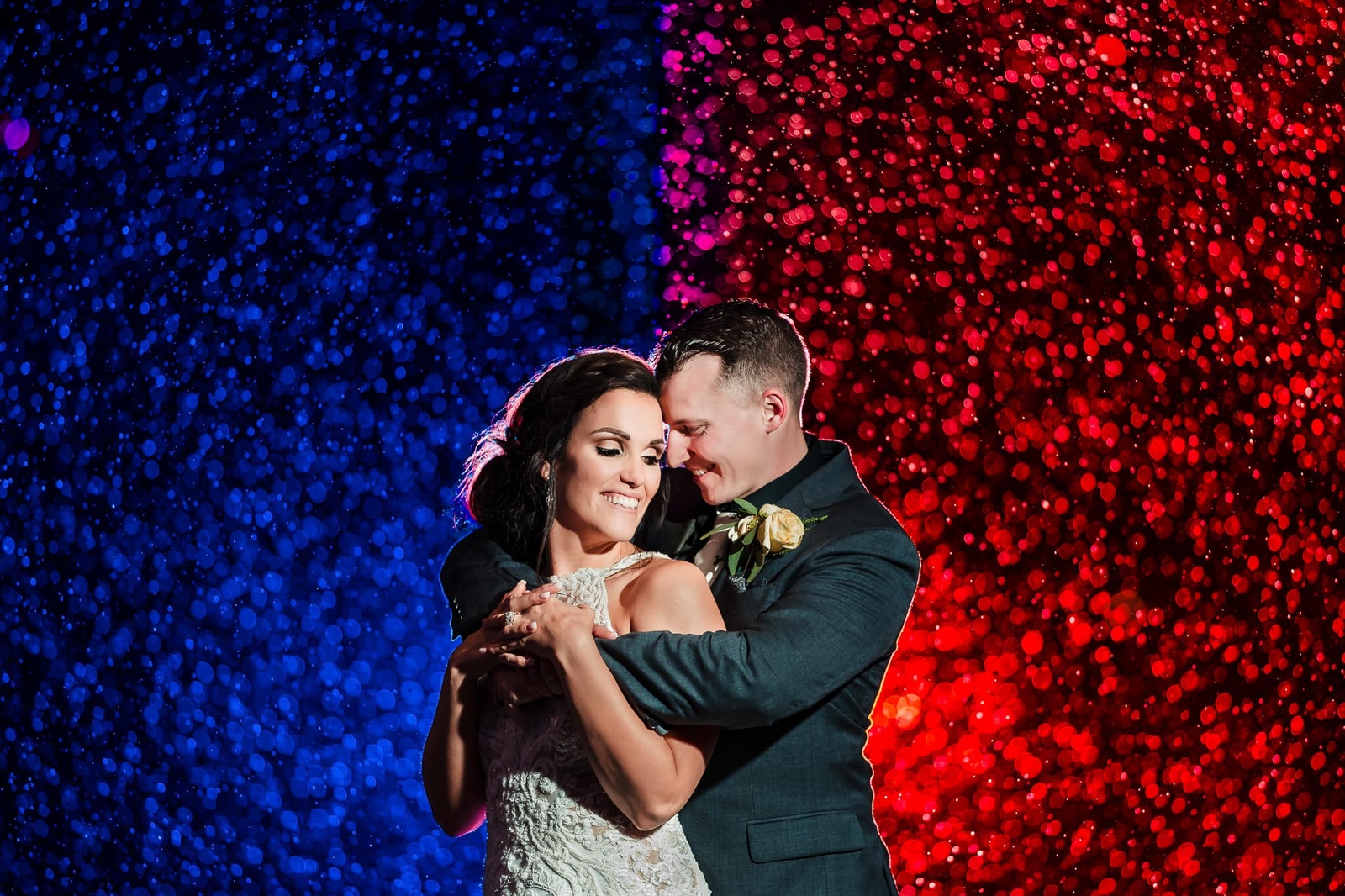 Groom with arms wrapped around bride in front of blue and red lights