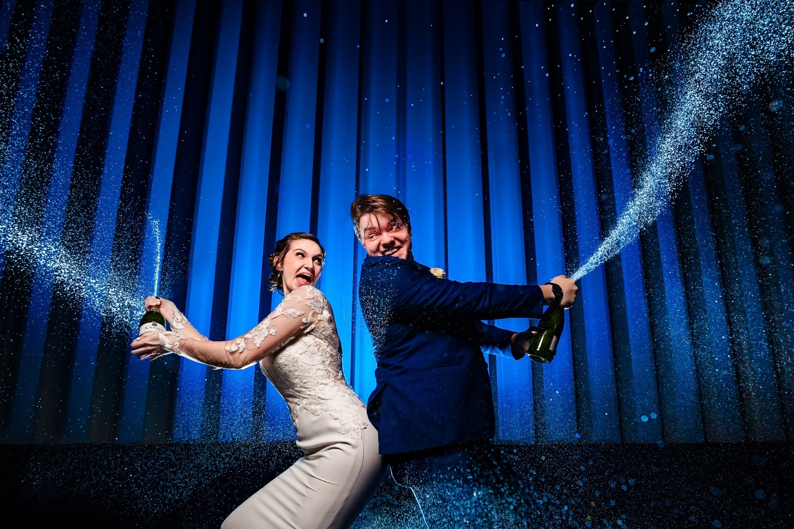 Bride and groom spraying champagne in front of blue background