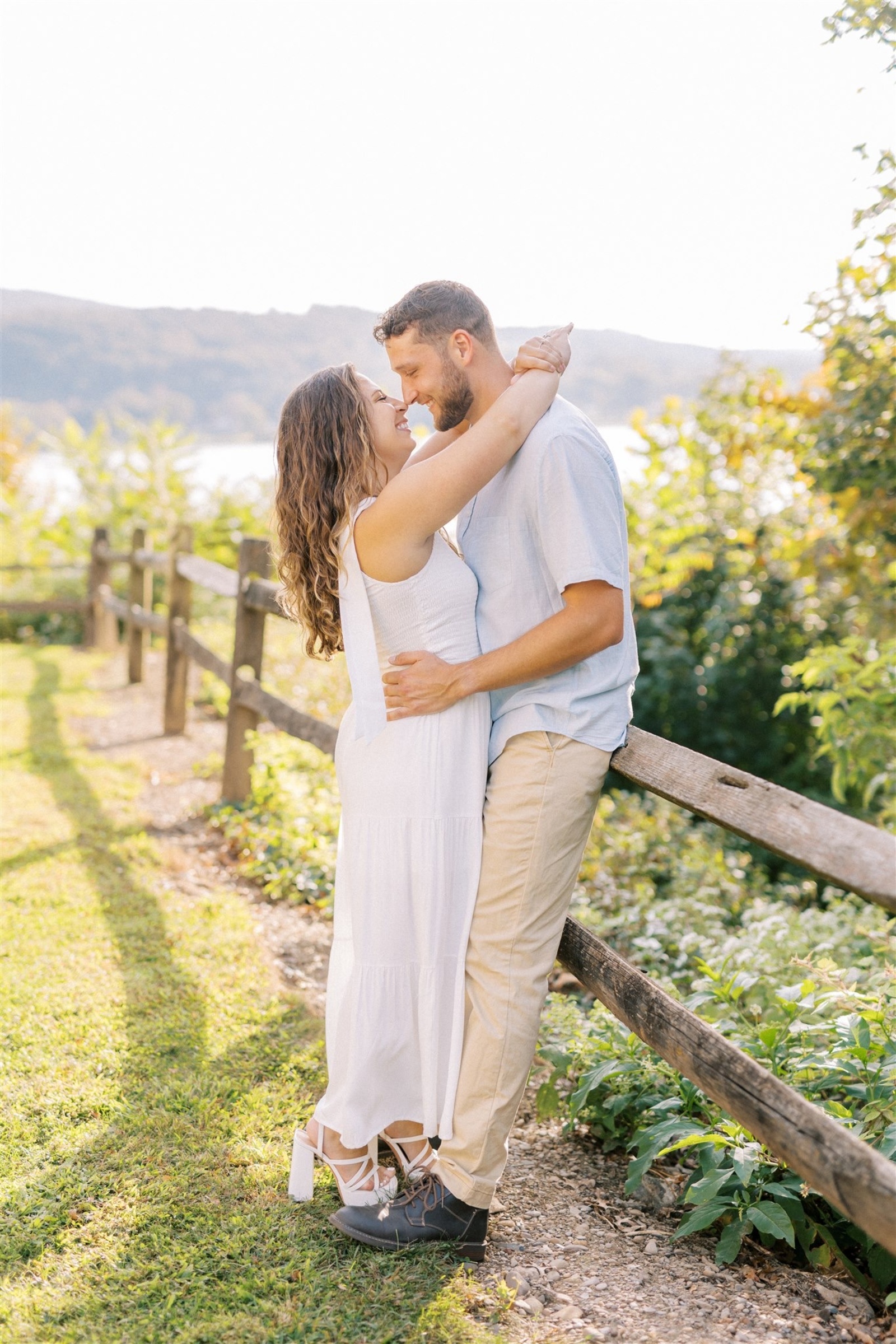 Couple embracing along a rustic wooden fence overlooking the Susquehanna River during sunset at Chickies Rock County Park in Lancaster County, Pennsylvania.