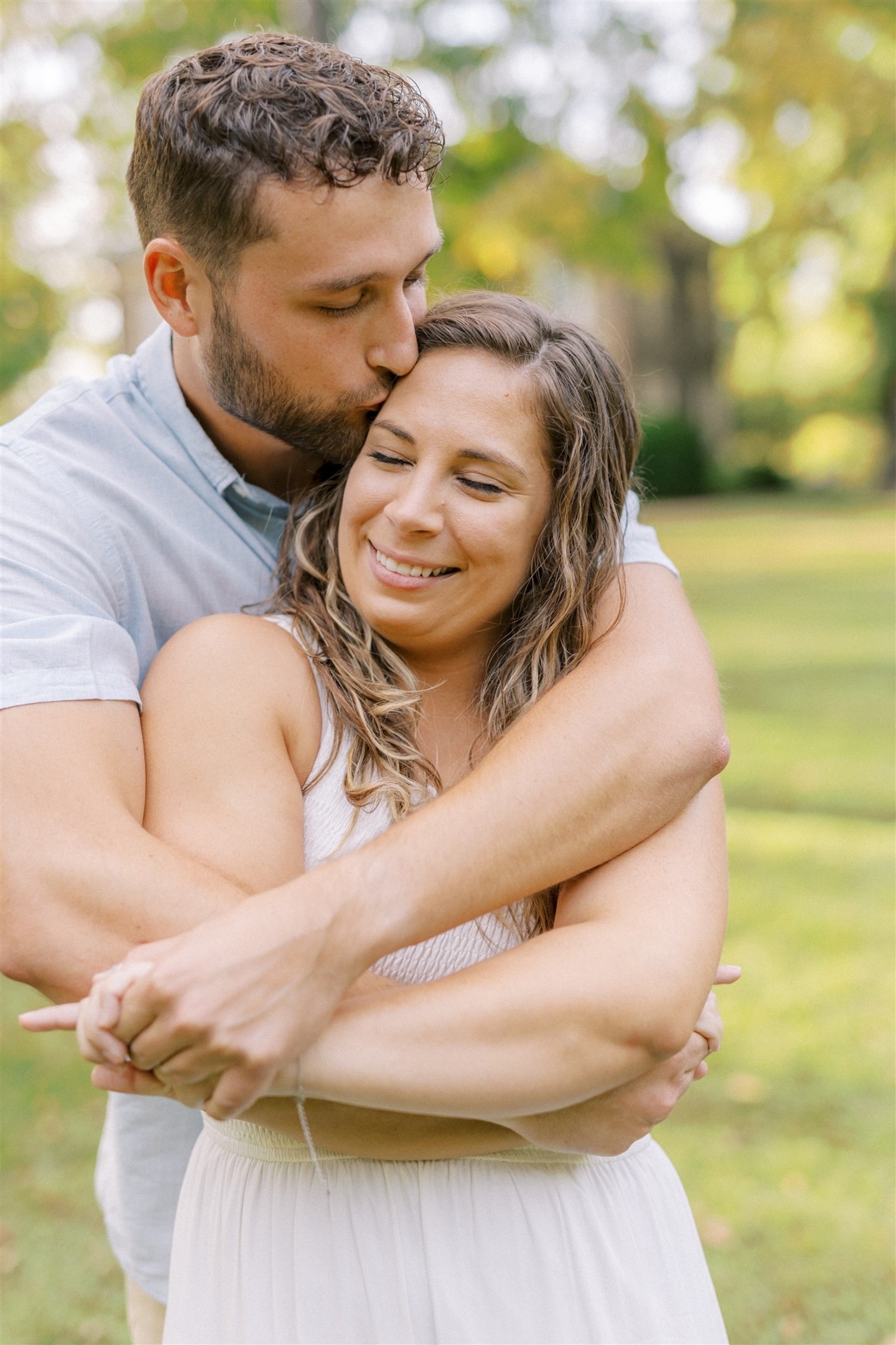 Couple sharing a quiet moment as he kisses her forehead during a romantic engagement session surrounded by greenery in Central Pennsylvania.