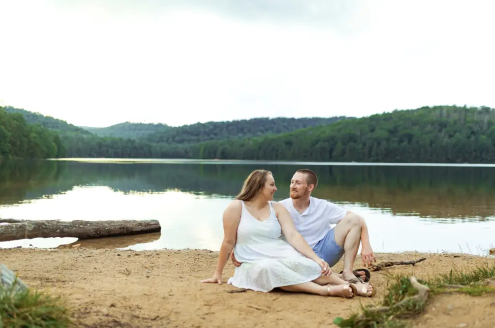 Couple sitting together on the sandy shoreline of Long Pine Run Reservoir in Caledonia State Park, surrounded by calm water and lush mountain views in Fayetteville, Pennsylvania.