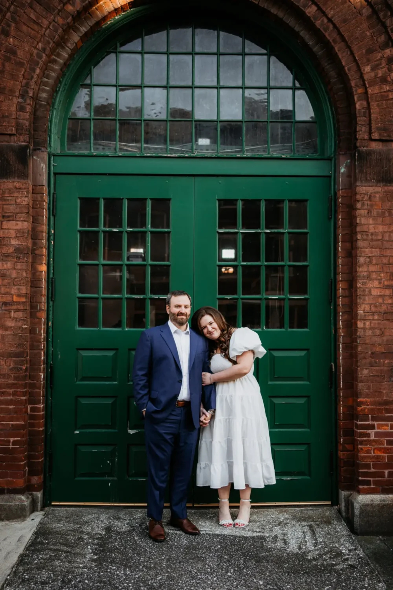Couple posing in front of a large green door of the historic brick Central Market building, blending classic and modern styles in their downtown York, PA engagement photos.