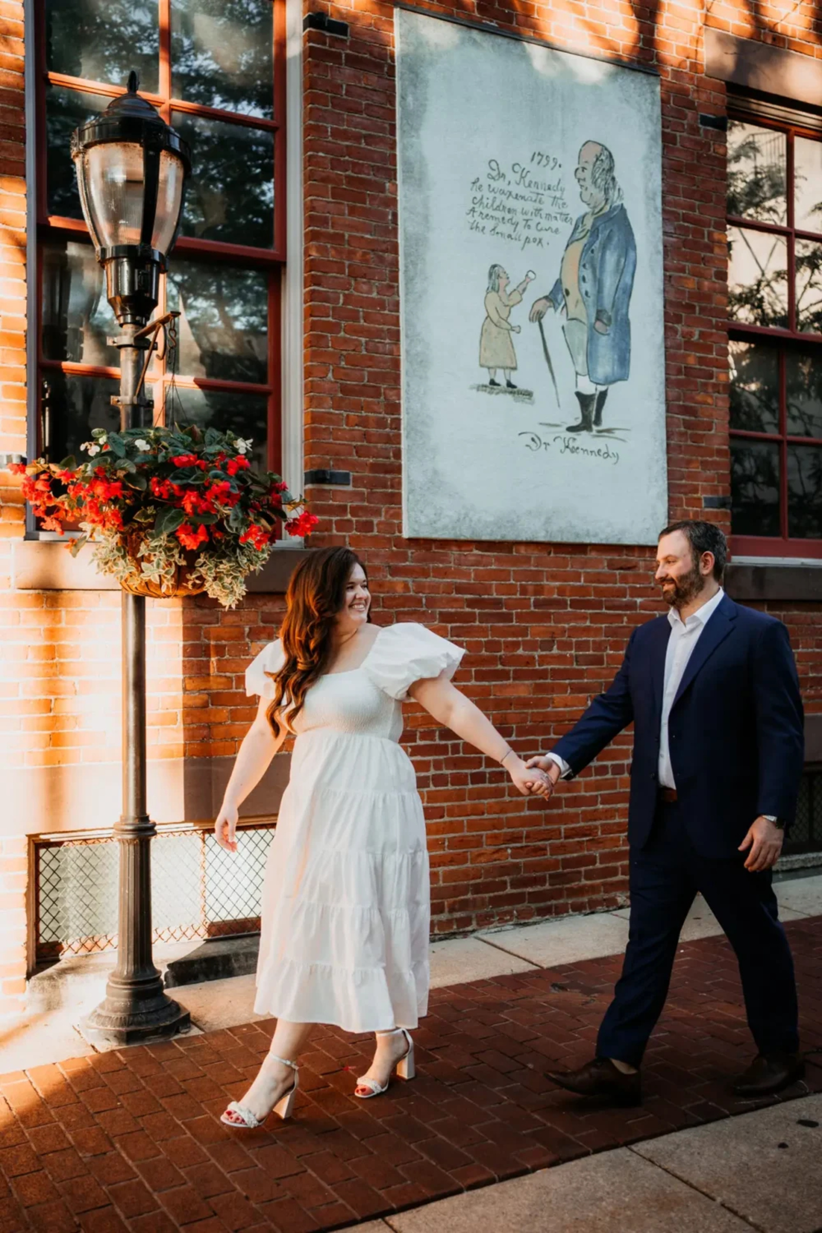 Couple holding hands and smiling while walking past a red brick building in downtown York, Pennsylvania during their engagement session.