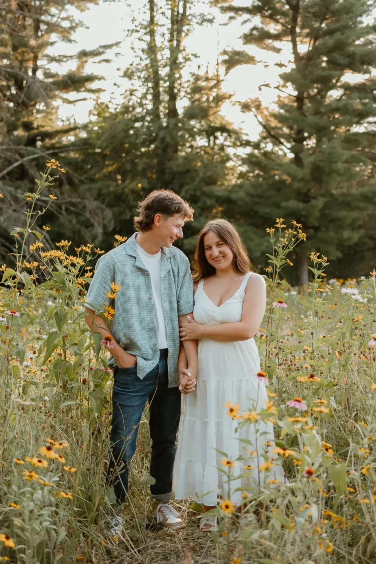 Couple standing in a field of yellow wildflowers at Sam Lewis State Park, smiling together during their summer engagement session overlooking the Susquehanna River in York County, Pennsylvania.