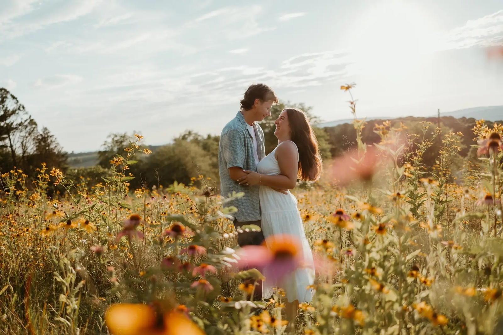 Couple laughing together in a meadow of wildflowers at sunset during their romantic engagement session at Sam Lewis State Park in Wrightsville, PA.