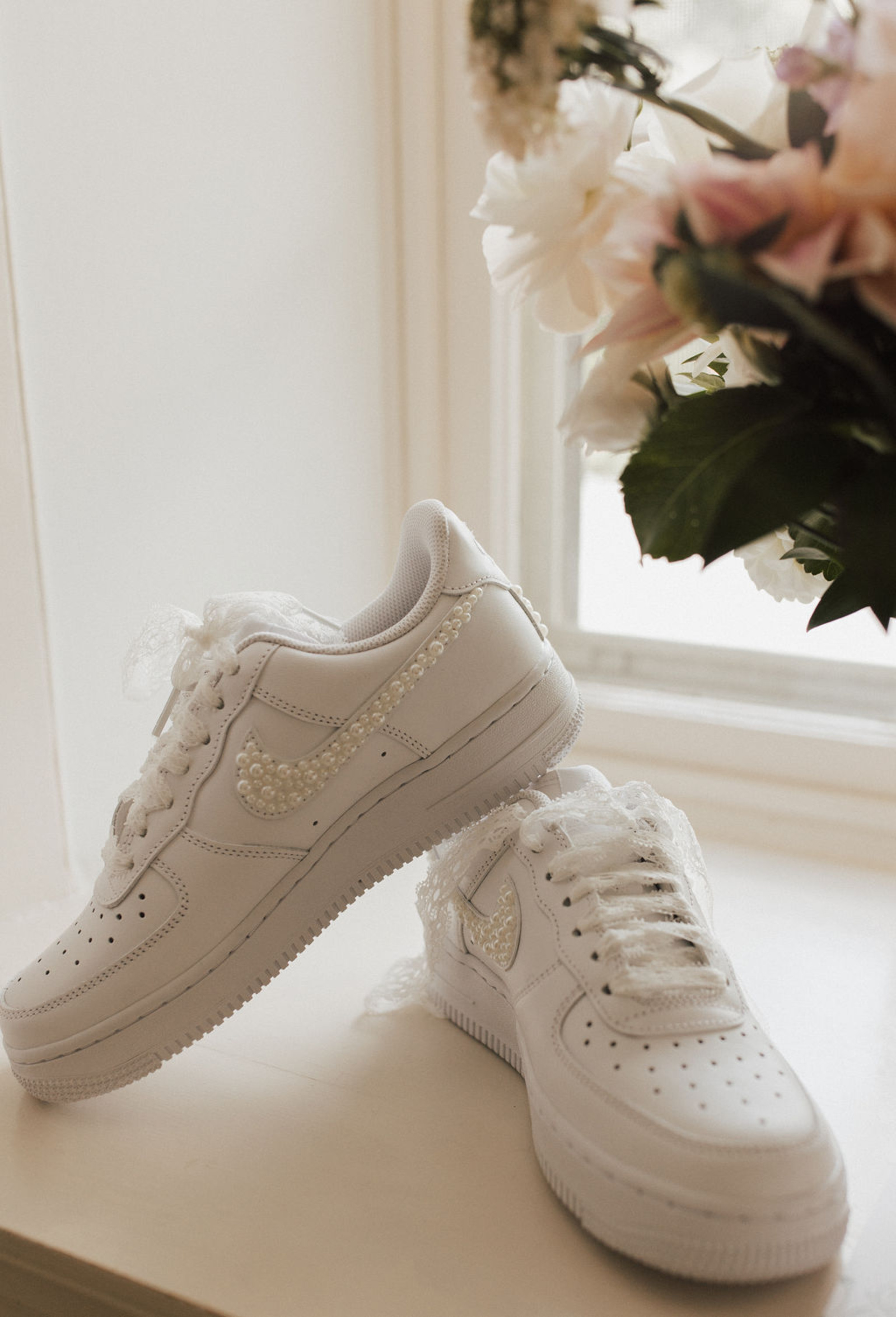 Pair of pearl embellished white Nike sneakers next to a pale pink and white bridal bouquet