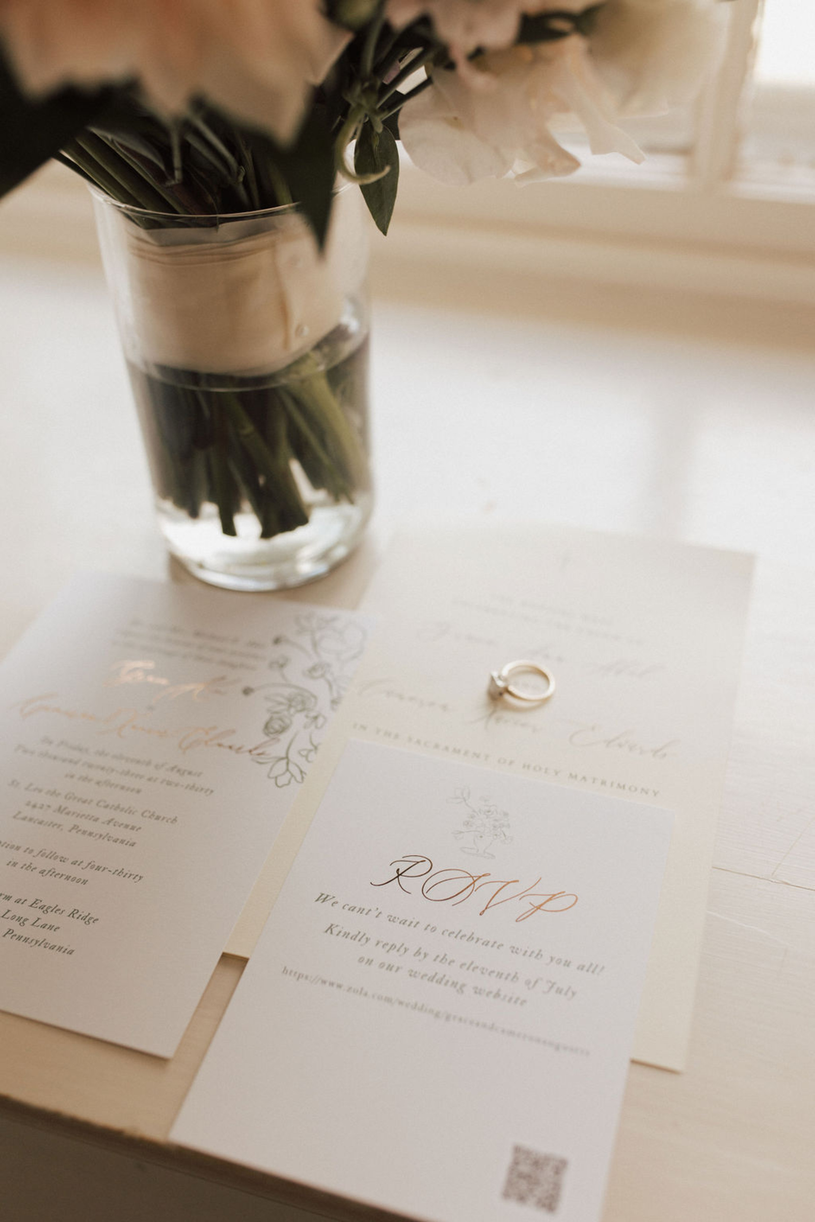 A gold diamond ring on top of a white wedding invitation with gold font