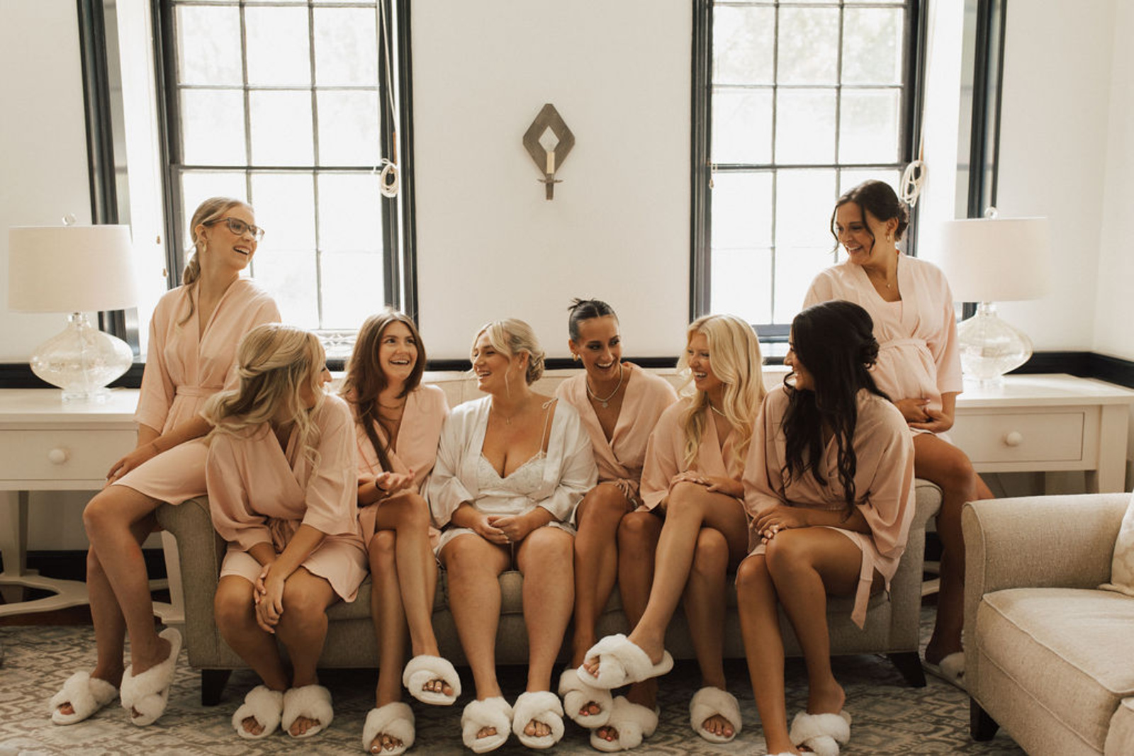 Bride and bridesmaids smiling and sitting on couch in matching robes and fuzzy slippers