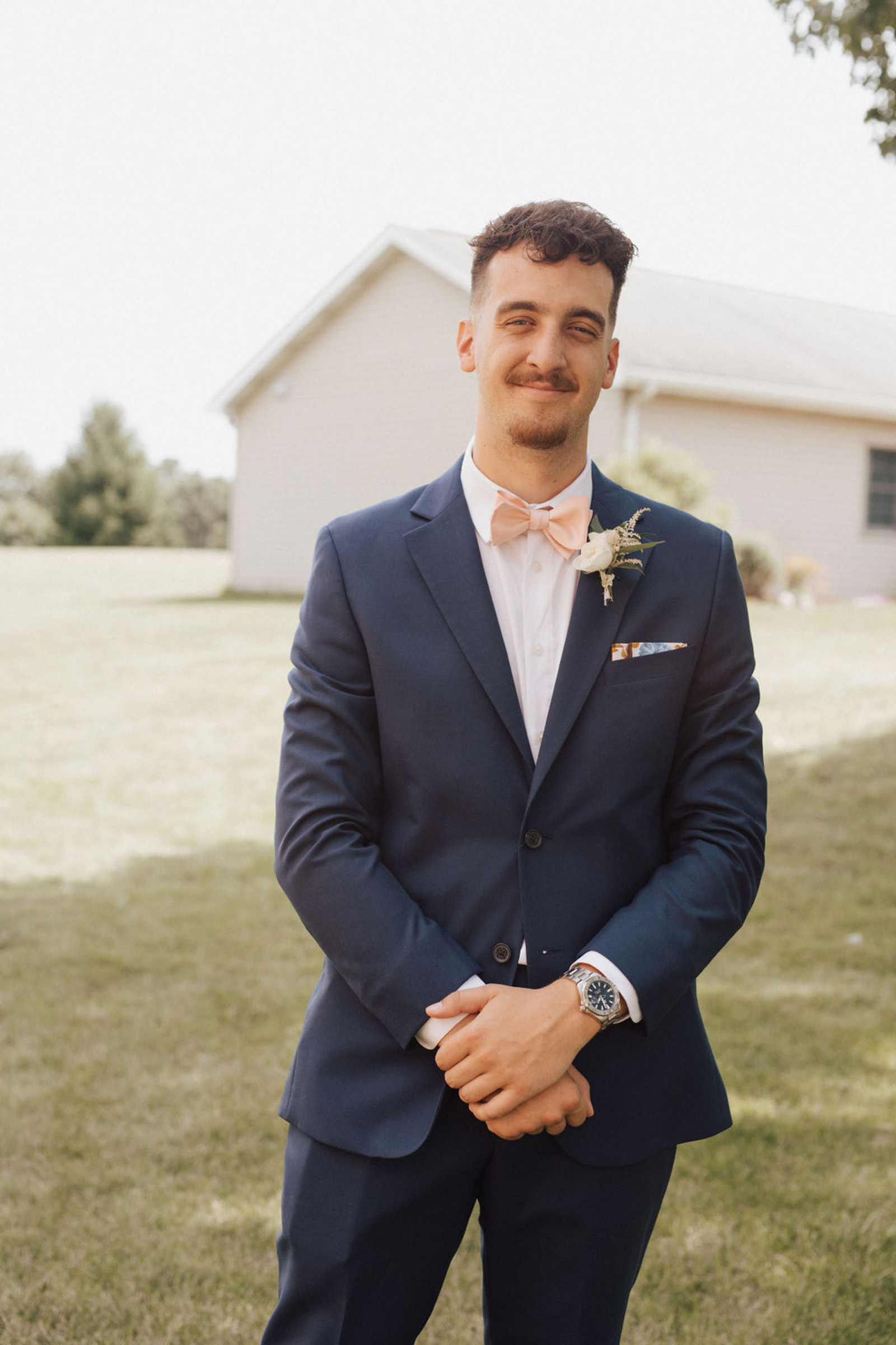 Central PA groom smiling with arms crossed while wearing navy blue suit, white dress shirt and light pink bow tie