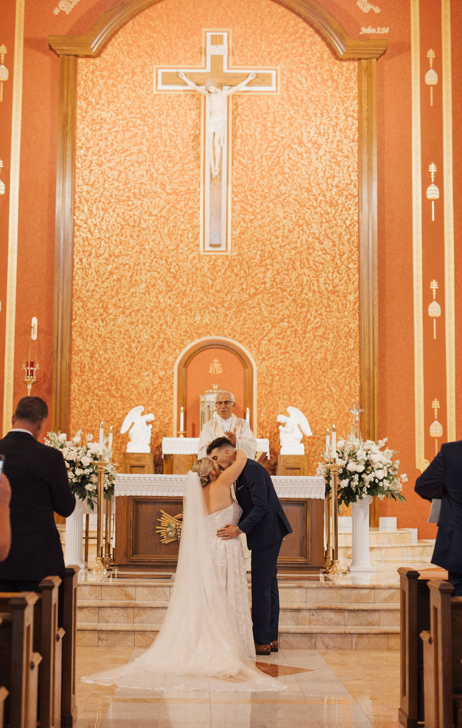 Central PA bride and groom kissing at the end of church aisle in front of priest and family and friends