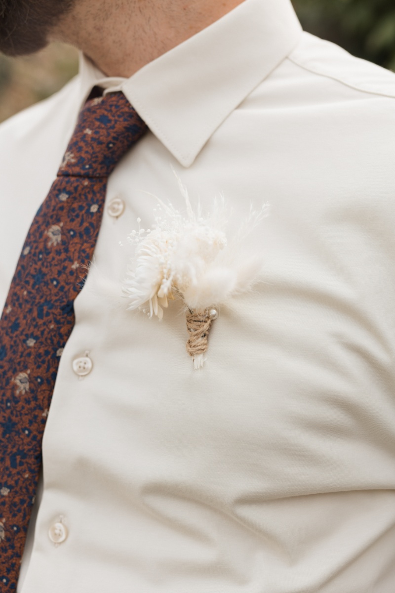 Groom wearing a neutral dried-flower boutonniere with twine and a rust-and-navy patterned tie for a fall wedding at St. Michael’s Vineyard.