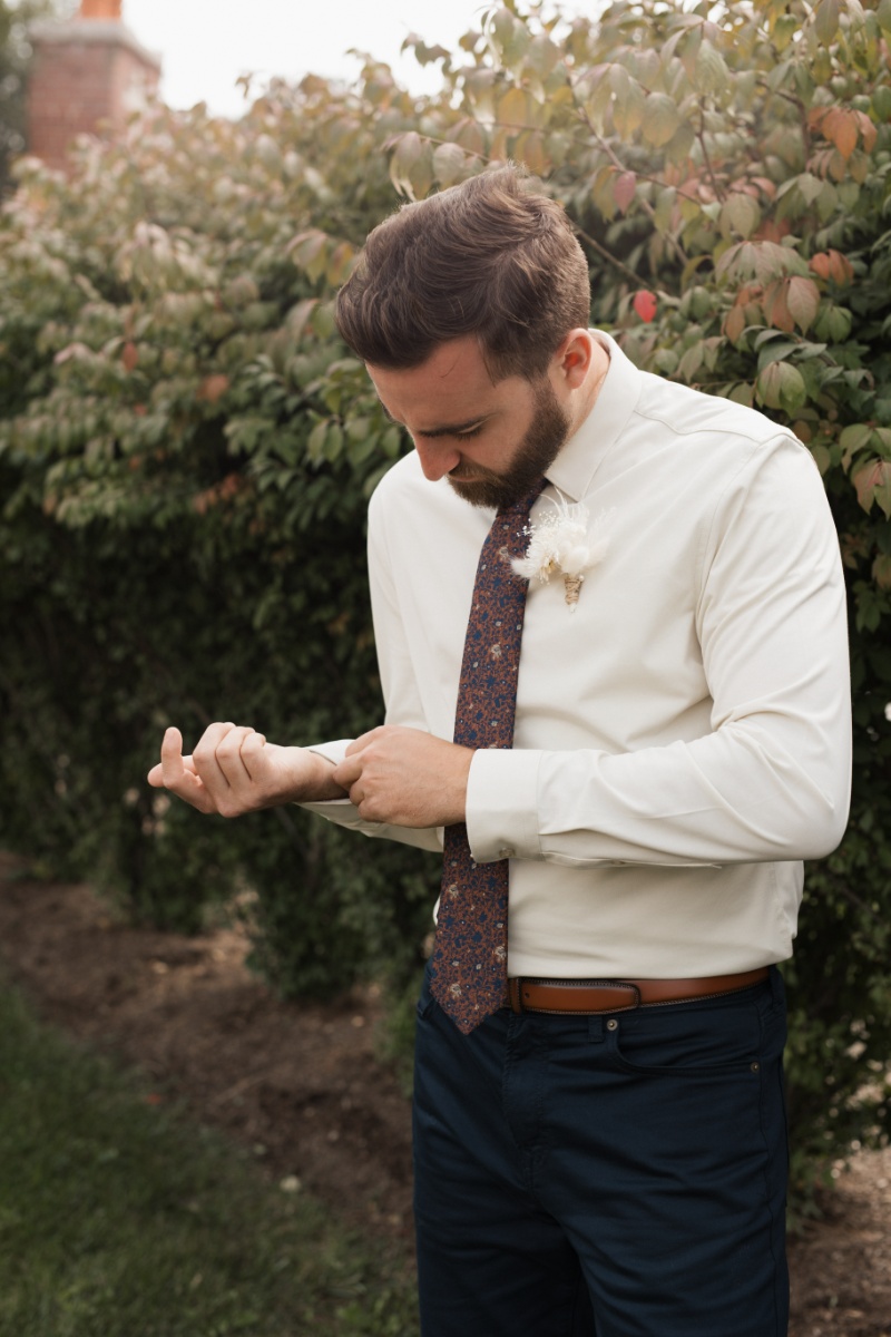 Groom adjusting his cuff before a fall wedding, wearing a patterned tie and neutral boutonniere at St. Michael’s Vineyard.