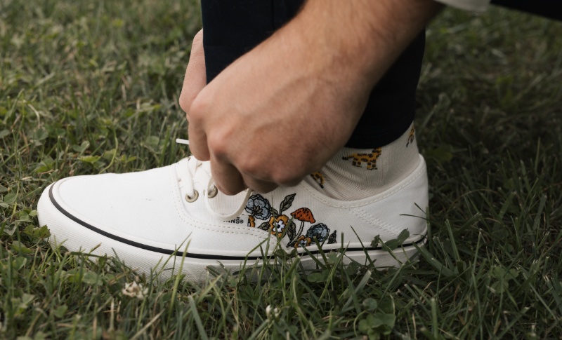 Groom tying white embroidered Vans sneakers featuring colorful mushroom details before his fall wedding at St. Michael’s Vineyard.