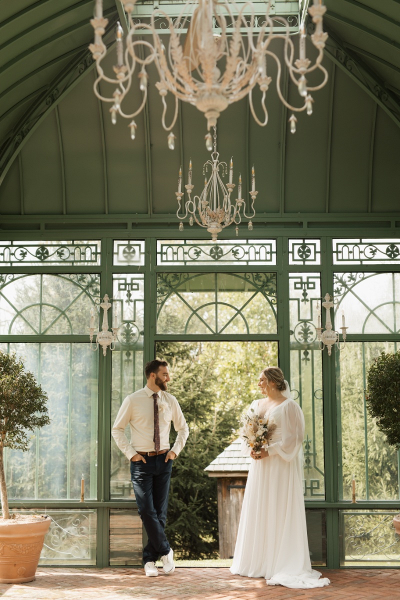 Bride and groom posing inside the ornate green glass greenhouse at St. Michael’s Vineyard during their fall wedding portraits.