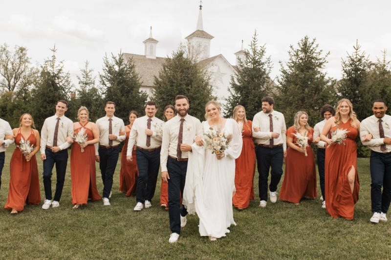 Bride and groom walking with their wedding party, including bridesmaids in rust dresses and groomsmen in neutral shirts, at St. Michael’s Vineyard.