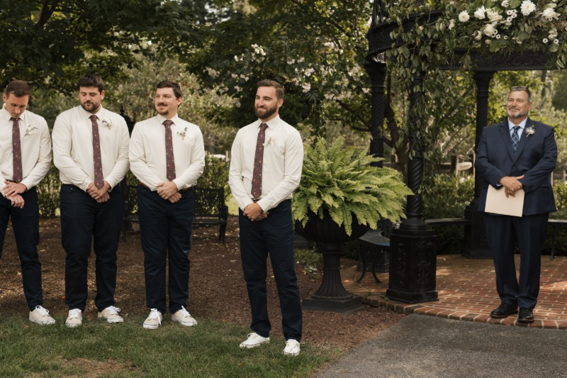 Groom standing with his groomsmen beneath the floral-covered garden gazebo during the wedding ceremony at St. Michael’s Vineyard.