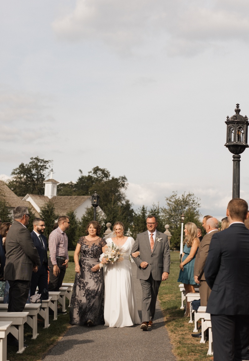 Bride walking down the outdoor ceremony aisle with family members during her fall wedding at St. Michael’s Vineyard in Pennsylvania.