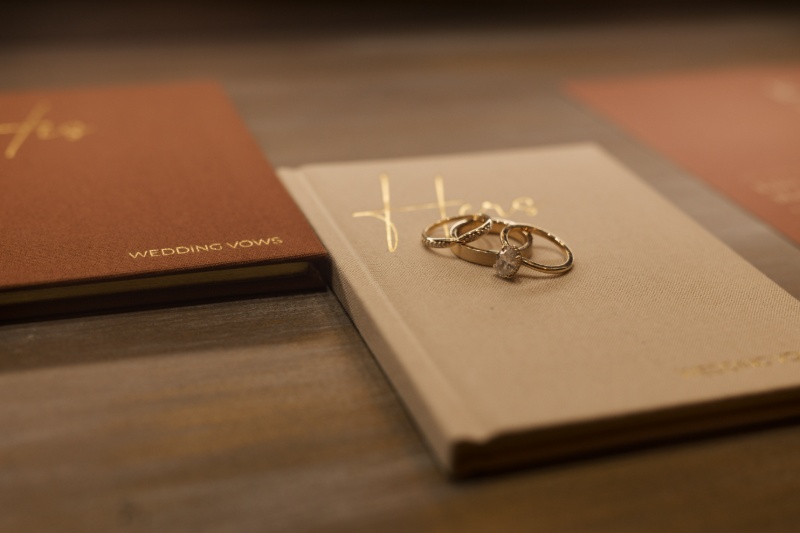 Wedding rings resting on personalized vow books in warm neutral tones during a fall wedding at St. Michael’s Vineyard.