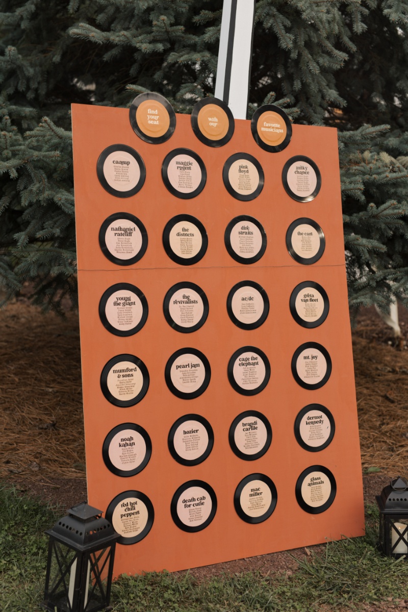 Music-themed wedding seating chart designed with vinyl record table assignments in warm rust tones.