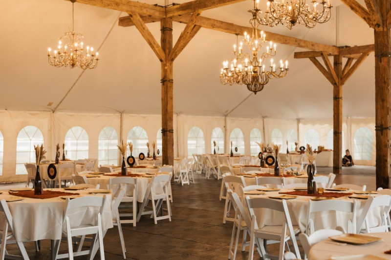 Fall wedding reception space at St. Michael’s Vineyard with chandeliers, exposed wood beams, white tables, and rust-colored details.