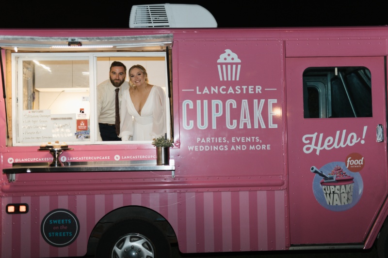 Bride and groom smiling from the window of the pink Lancaster Cupcake truck during their wedding reception.