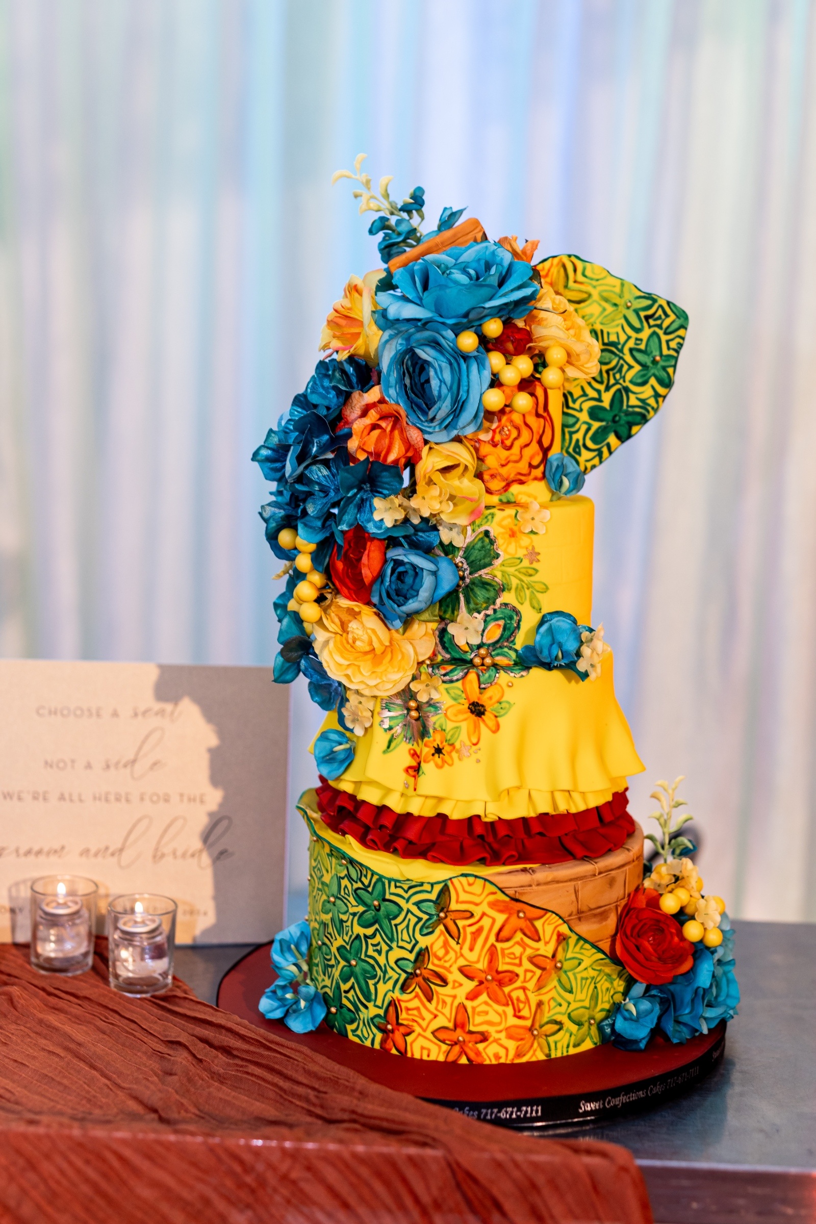 Full view of a vibrant yellow wedding cake with cascading blue and yellow flowers, surrounded by candles and decor inspired by West Side Story.