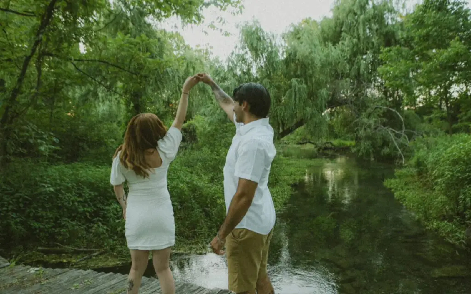 Couple twirling together on a wooden dock surrounded by lush greenery and the peaceful stream at Letort Spring Garden Preserve in Carlisle, Pennsylvania.