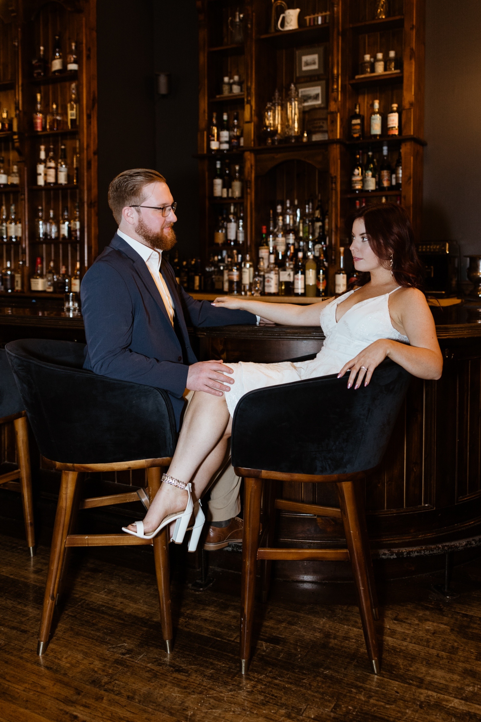 Couple dressed elegantly enjoying cocktails together at a dimly lit bar during their stylish engagement session in Central Pennsylvania.
