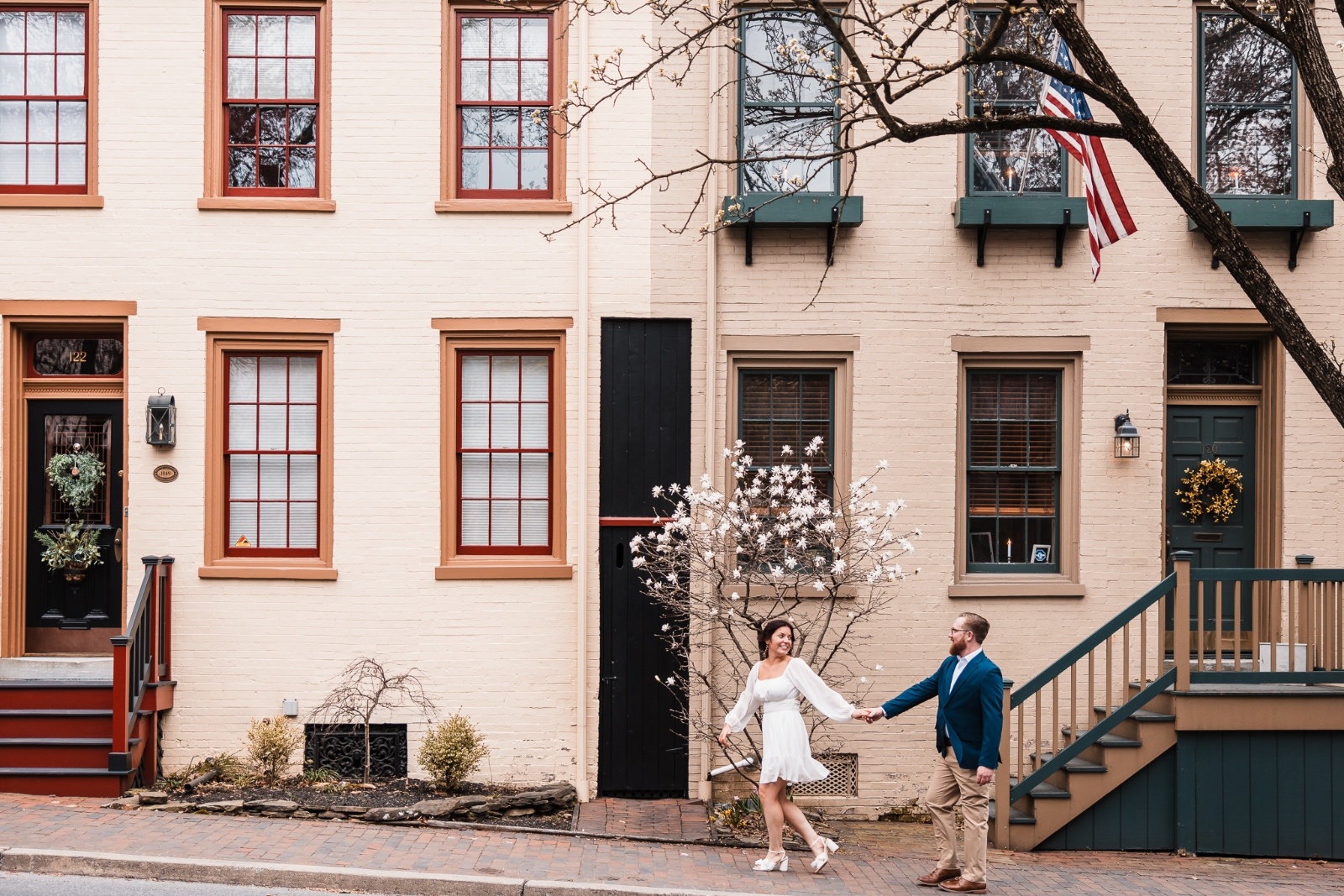 Couple walking hand-in-hand past charming brick rowhomes and blooming magnolia trees in downtown Lancaster, Pennsylvania.