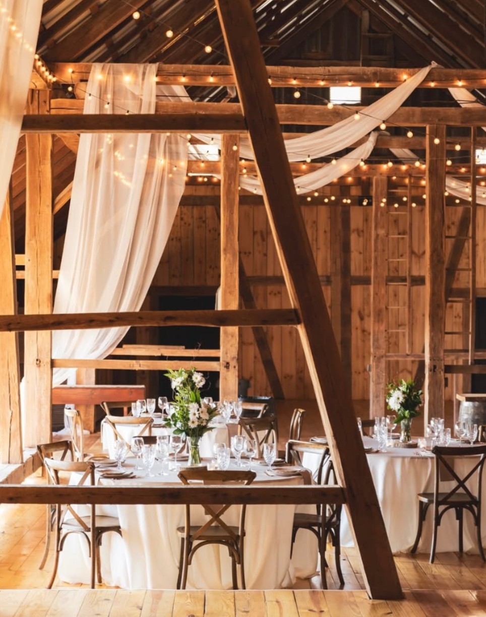 Rustic barn at the Barn at Hill Country wedding reception with exposed wood beams, string lights, white draping and floral centerpieces.