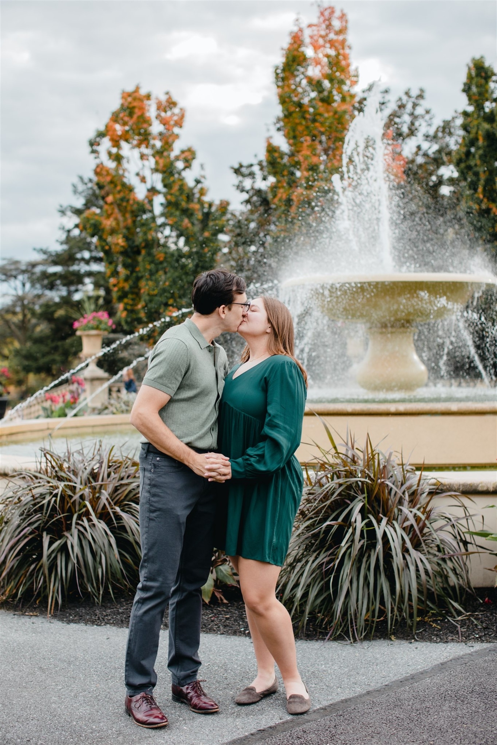 Couple sharing a kiss in front of the grand fountain surrounded by lush gardens at Masonic Village in Elizabethtown, Pennsylvania during their fall engagement session.