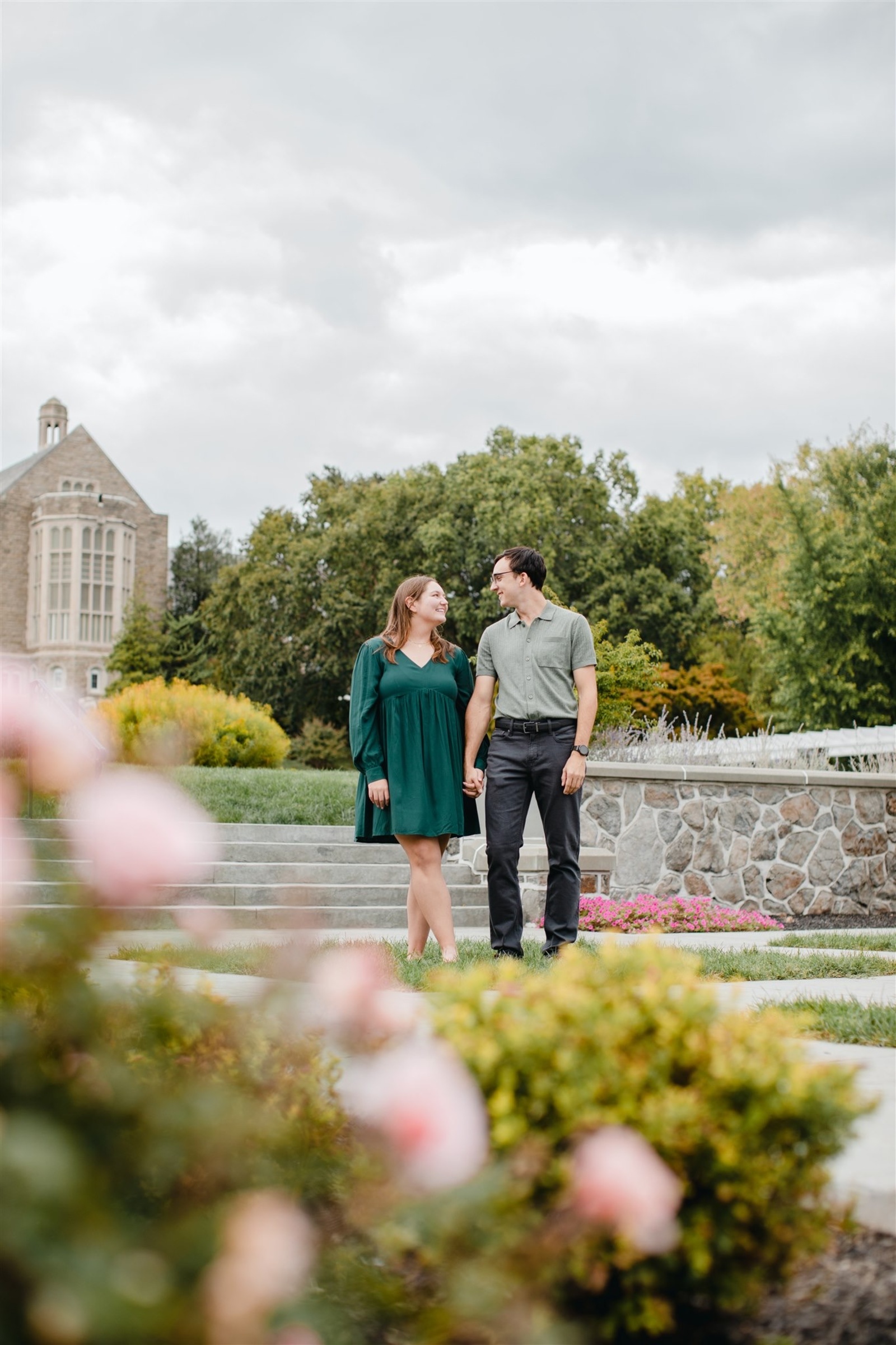 Couple walking hand-in-hand through the manicured gardens of Masonic Village with historic stone architecture in the background during their Central Pennsylvania engagement photos.