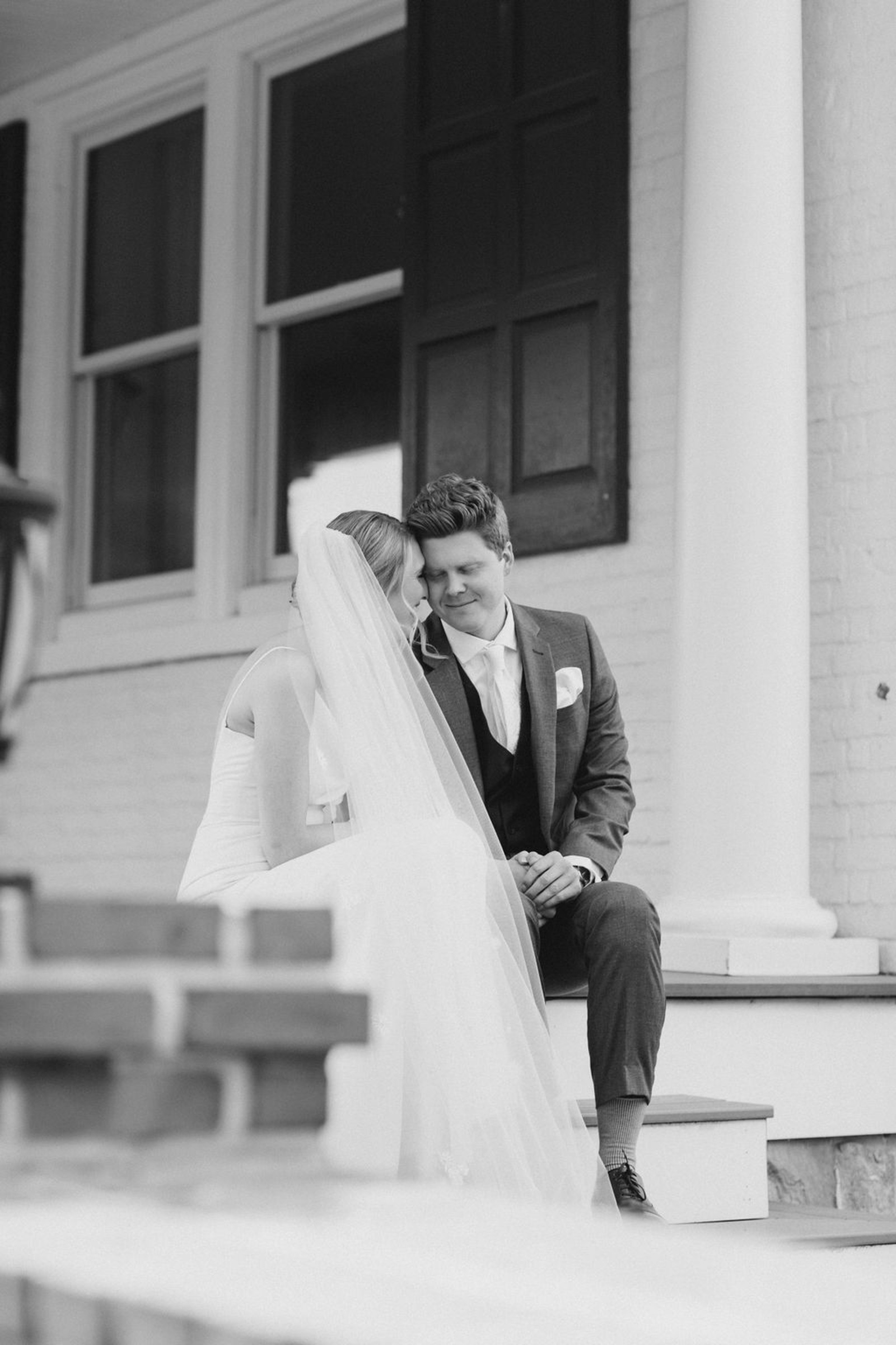 A black-and-white photo of the bride and groom sitting closely on the steps of Historic Ashland, sharing an intimate and quiet moment together before their ceremony.