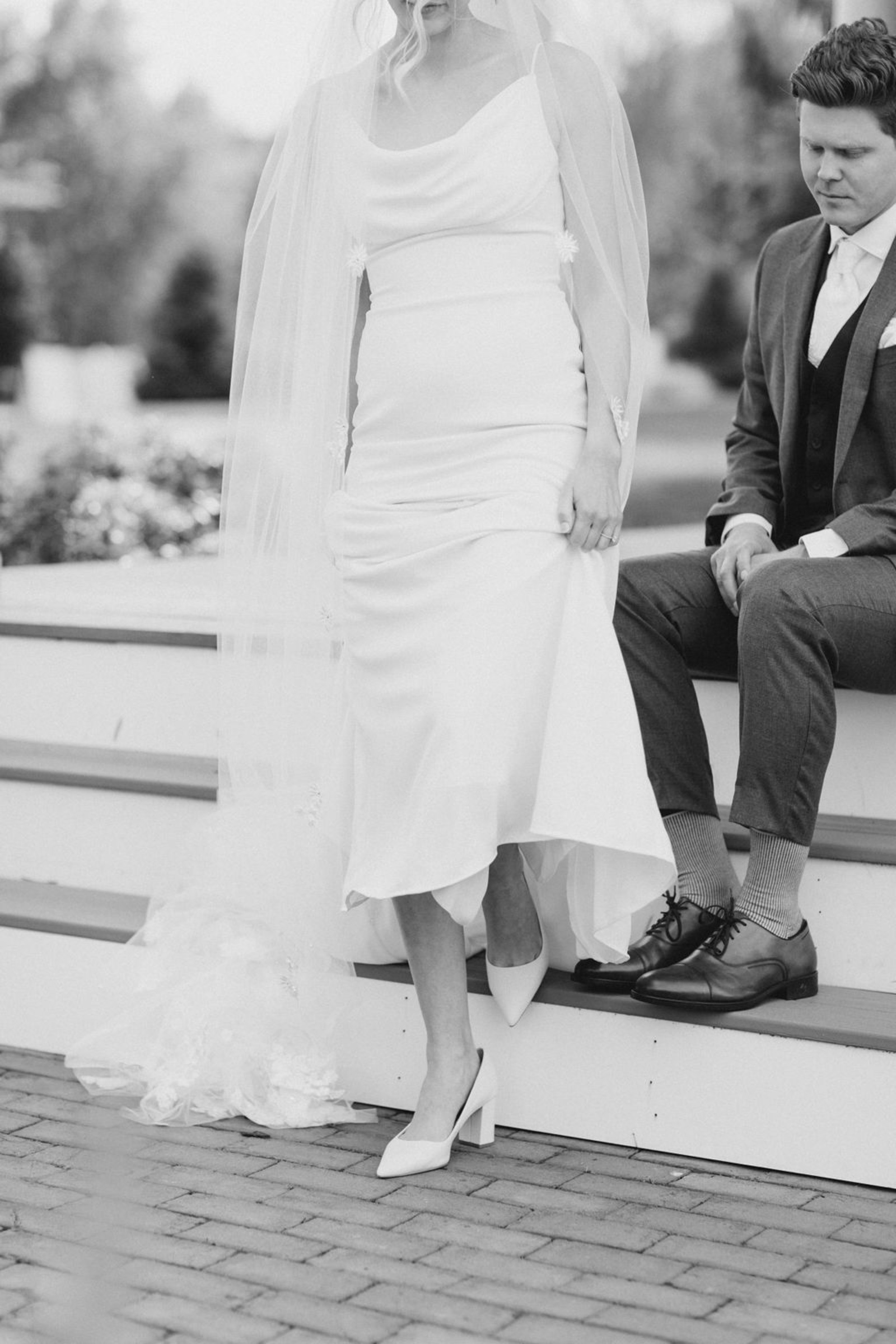 A close-up black-and-white shot of the bride’s satin wedding gown and pointed heels as she stands gracefully beside the groom on the steps of Historic Ashland.