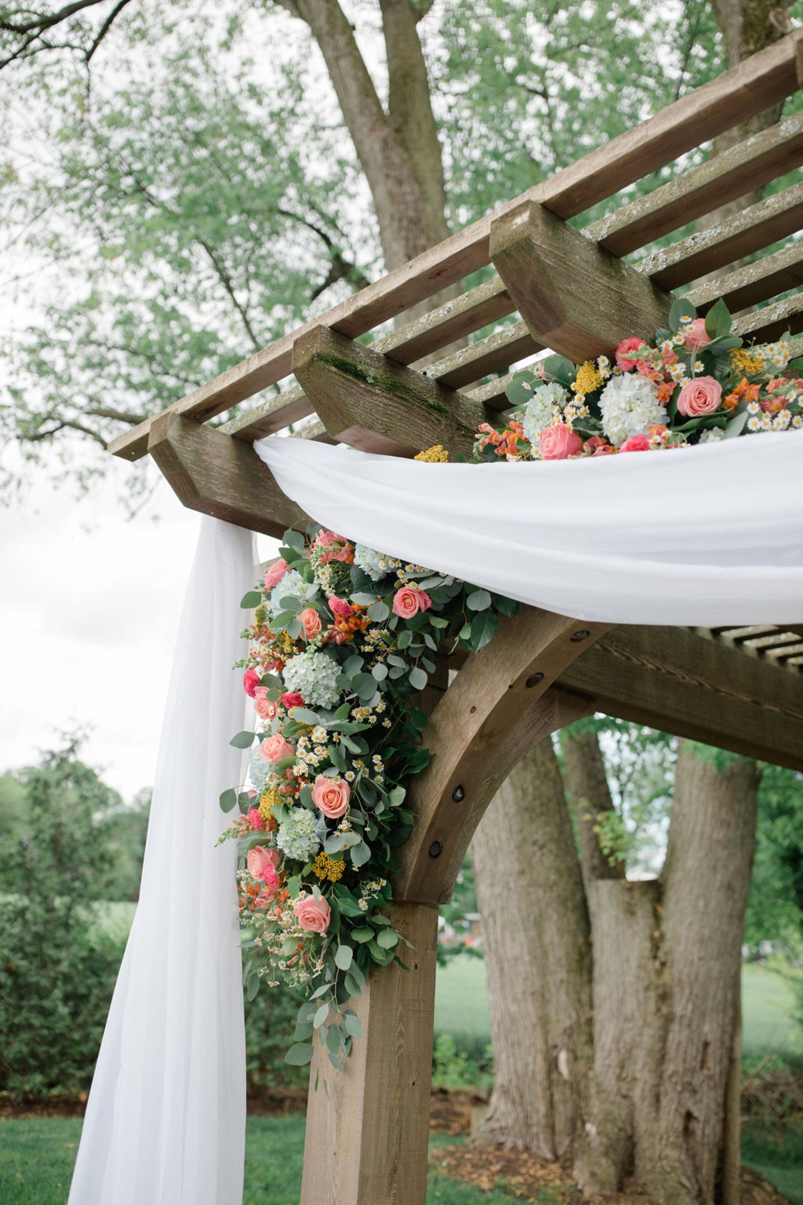 Close-up of colorful floral installation with roses, hydrangeas, and greenery draped across the wooden arbor at Historic Ashland.