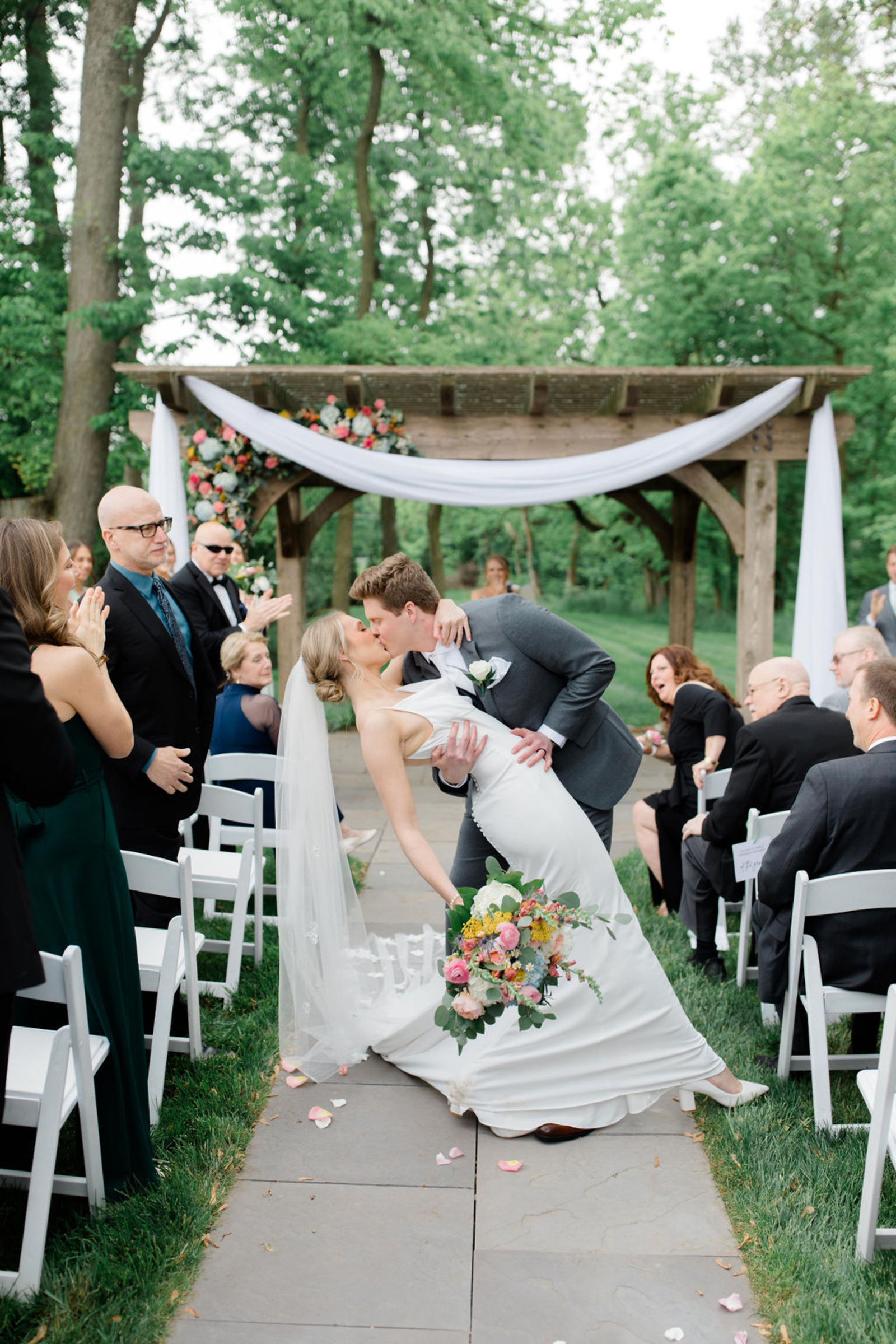 Newlyweds share a joyful kiss down the aisle surrounded by family and friends beneath the floral-decorated arbor at Historic Ashland.