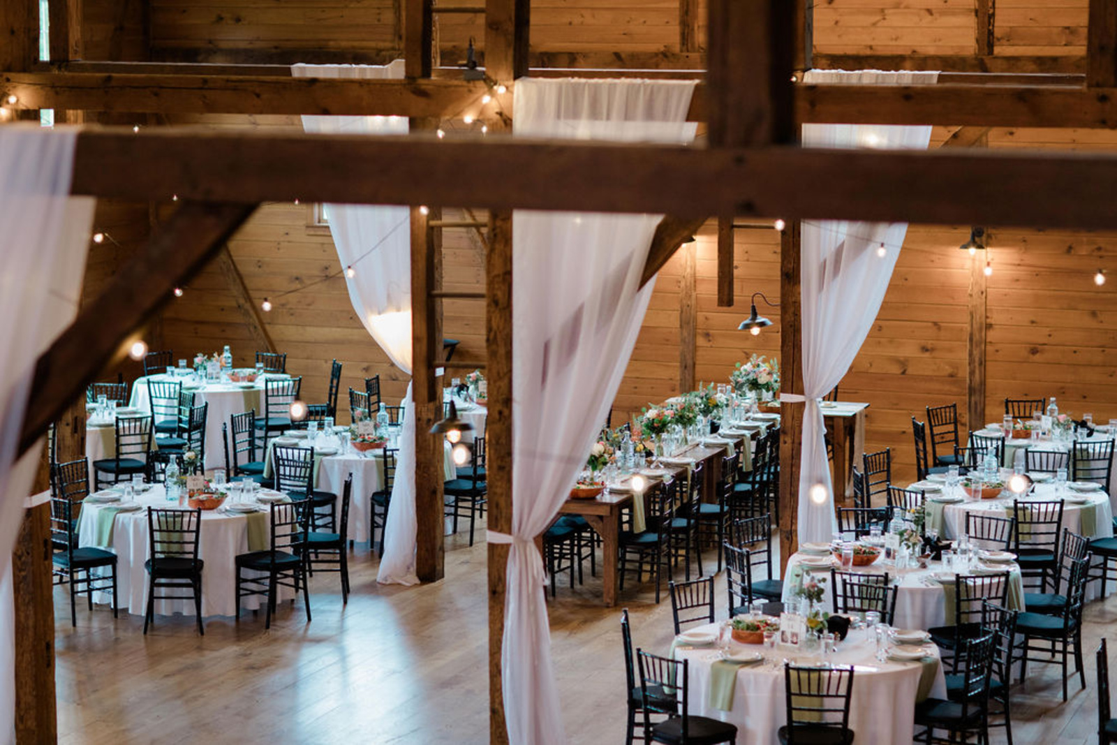 Rustic barn reception at Historic Ashland with draped white fabric, string lights, and floral centerpieces on round and banquet tables.