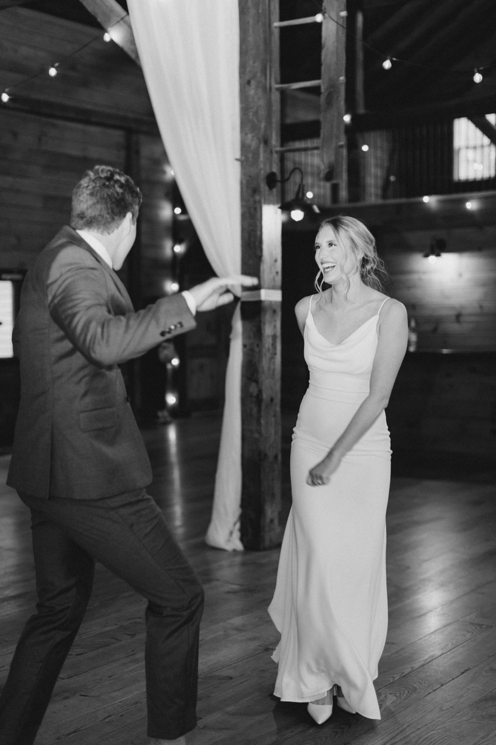 Bride and groom share a joyful first dance under string lights inside Historic Ashland’s barn venue.