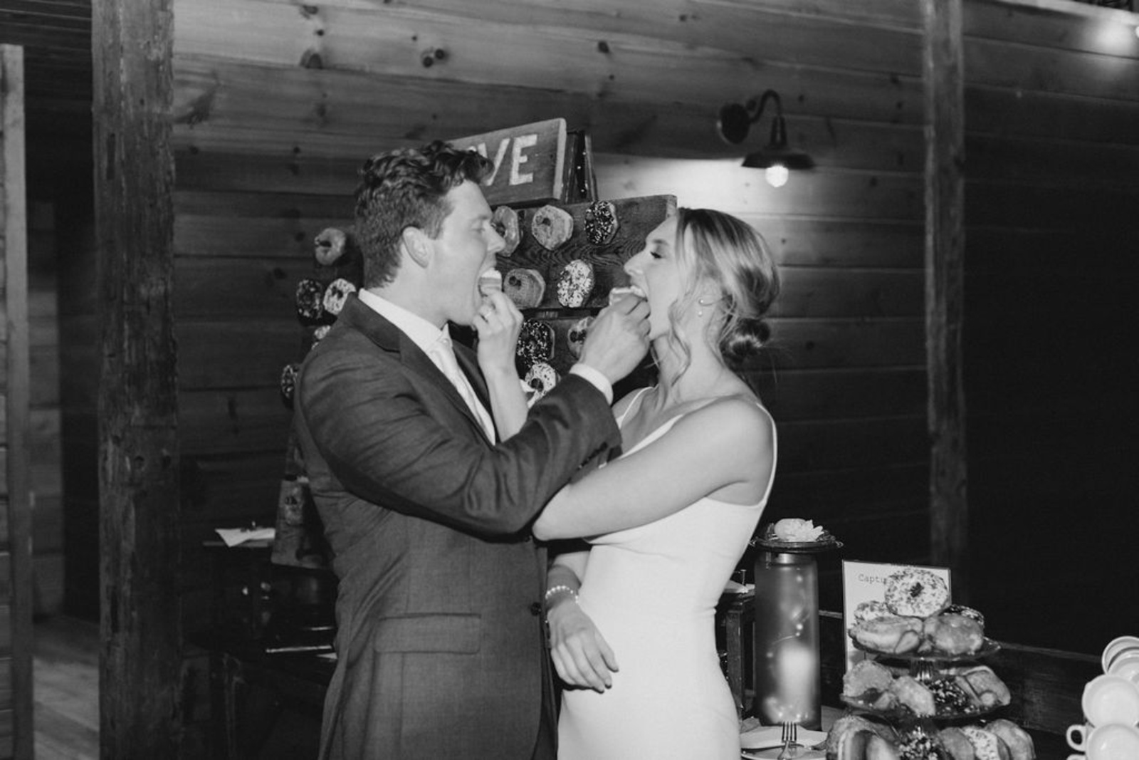 Couple laughs while feeding each other donuts from their dessert wall at their Historic Ashland wedding reception.