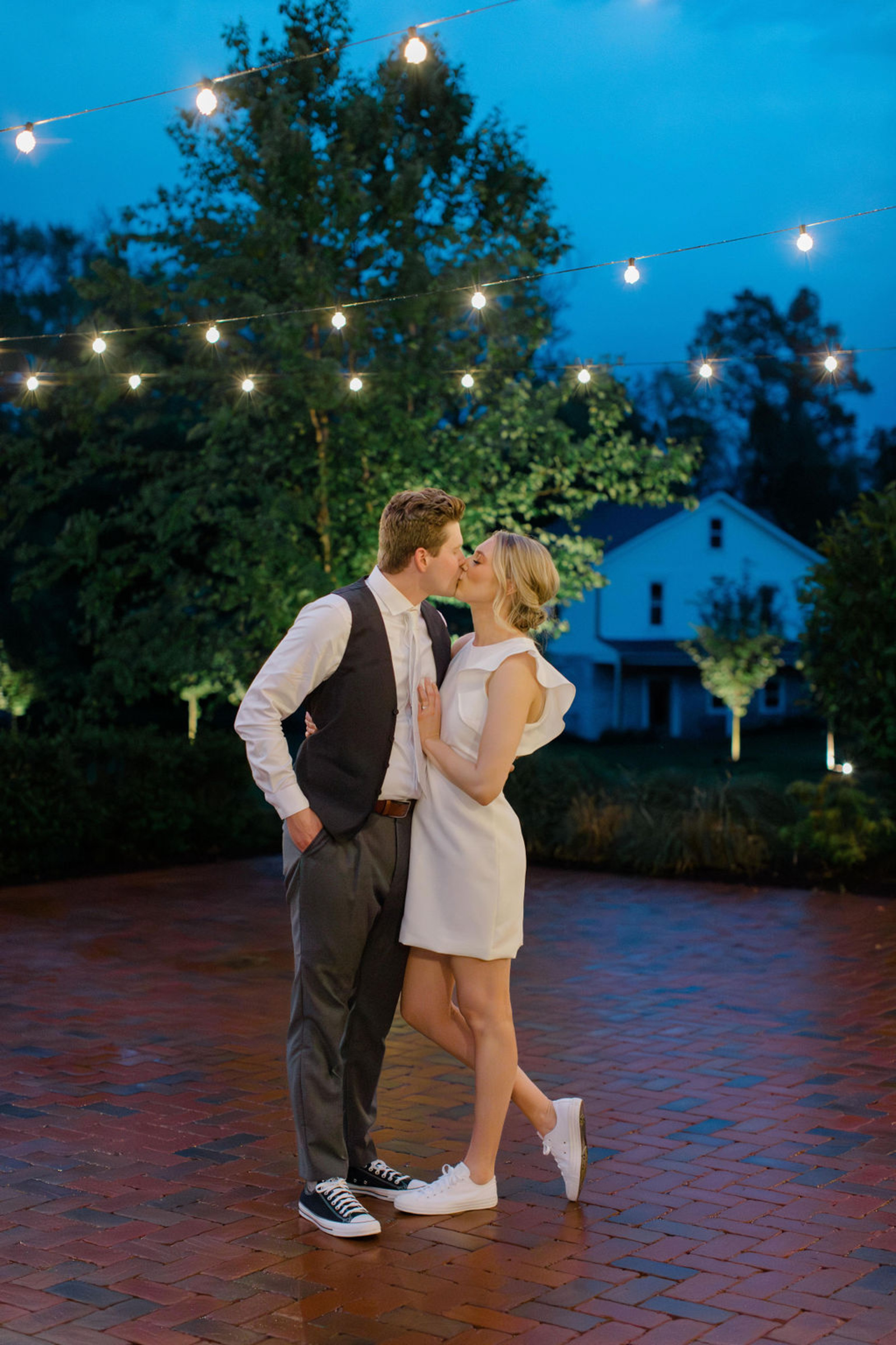 Bride and groom share a kiss beneath glowing string lights during their wedding evening at Historic Ashland in Central Pennsylvania.