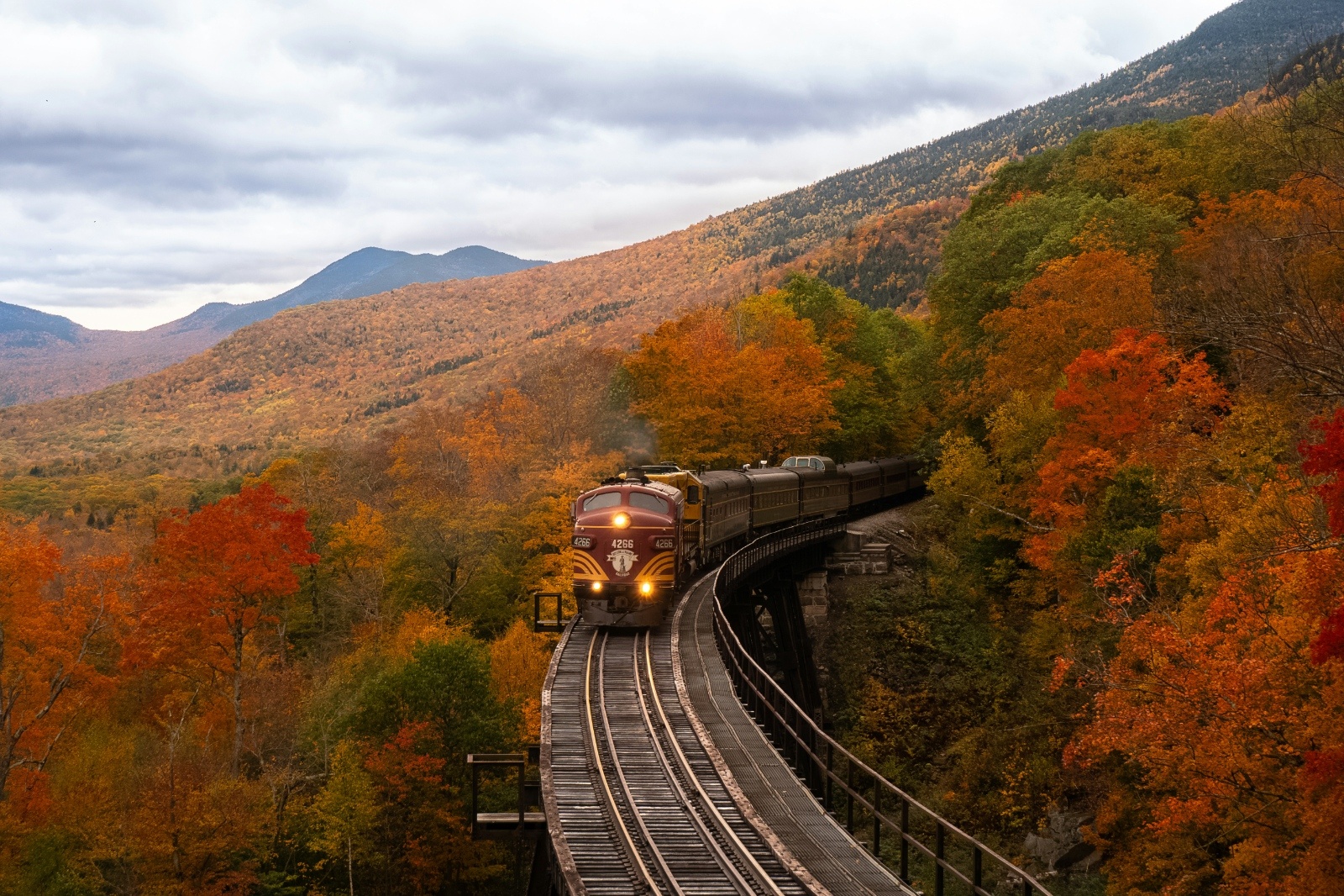 A vintage train winds through the colorful fall foliage and mountain landscape of Jim Thorpe, Pennsylvania — a cozy, picturesque bachelorette weekend destination for nature lovers.