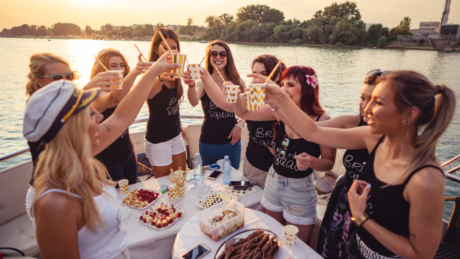 A group of women wearing matching “Bride Squad” shirts toast drinks together on a boat during sunset in Annapolis, Maryland — celebrating a nautical-themed bachelorette weekend on the Chesapeake Bay.