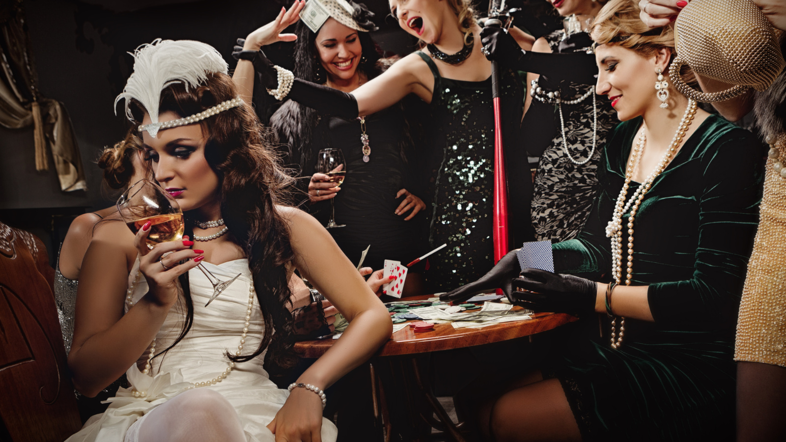 Women dressed in vintage flapper-inspired outfits with pearls, feathers, and sequins enjoy drinks and cards at a casino-style table — capturing the glitz and nightlife energy of an Atlantic City bachelorette getaway.